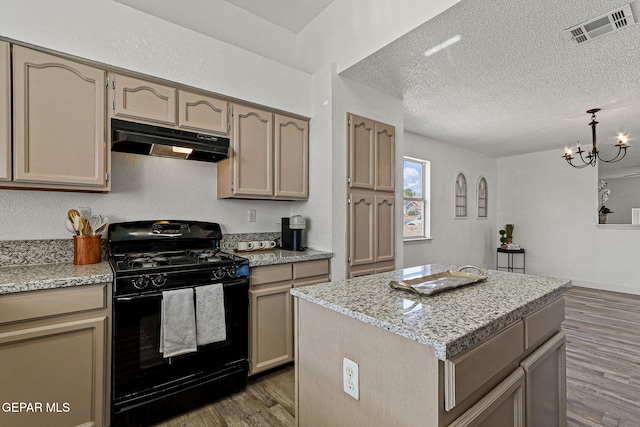 kitchen with wood finished floors, visible vents, black gas range, under cabinet range hood, and a textured ceiling