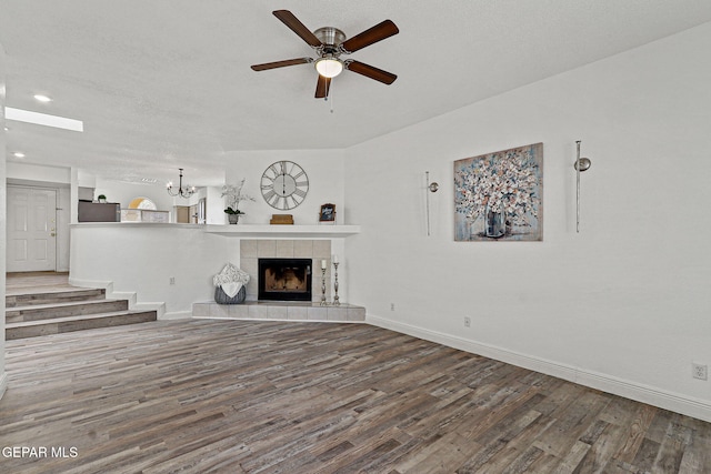 unfurnished living room with ceiling fan with notable chandelier, a tile fireplace, baseboards, and wood finished floors