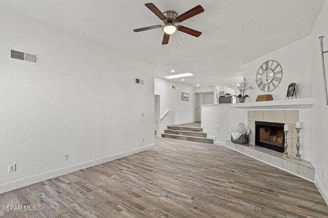 unfurnished living room with visible vents, a ceiling fan, wood finished floors, stairway, and a fireplace