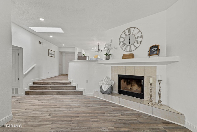 unfurnished living room featuring a tile fireplace, a textured ceiling, a skylight, and wood finished floors