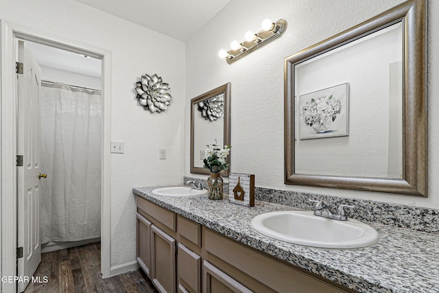 full bathroom featuring double vanity, wood finished floors, a textured wall, and a sink