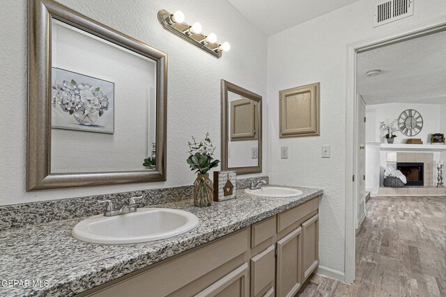 ensuite bathroom featuring visible vents, a tile fireplace, wood finished floors, and a sink