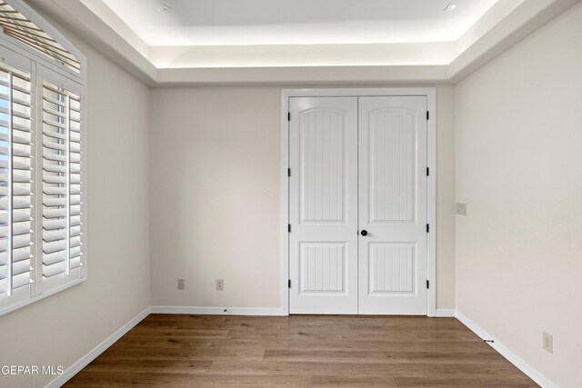 unfurnished bedroom with a tray ceiling, wood finished floors, a closet, and baseboards