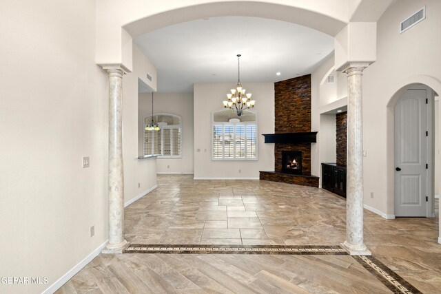 unfurnished living room with baseboards, a stone fireplace, a chandelier, arched walkways, and ornate columns