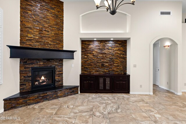unfurnished living room featuring a high ceiling, a fireplace, baseboards, arched walkways, and a chandelier