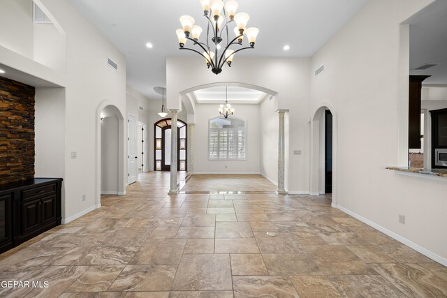 unfurnished living room featuring arched walkways, stone tile floors, baseboards, a chandelier, and recessed lighting