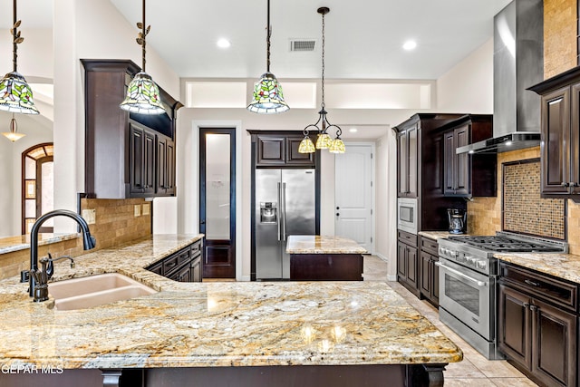 kitchen with stainless steel appliances, wall chimney exhaust hood, a sink, light stone countertops, and dark brown cabinets