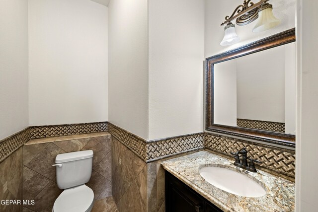half bathroom featuring tile walls, toilet, a wainscoted wall, and vanity