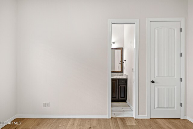 unfurnished bedroom with light wood-style flooring, baseboards, and ensuite bath