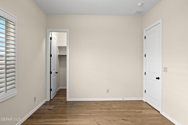 unfurnished bedroom with wood finished floors, baseboards, a walk in closet, and a closet