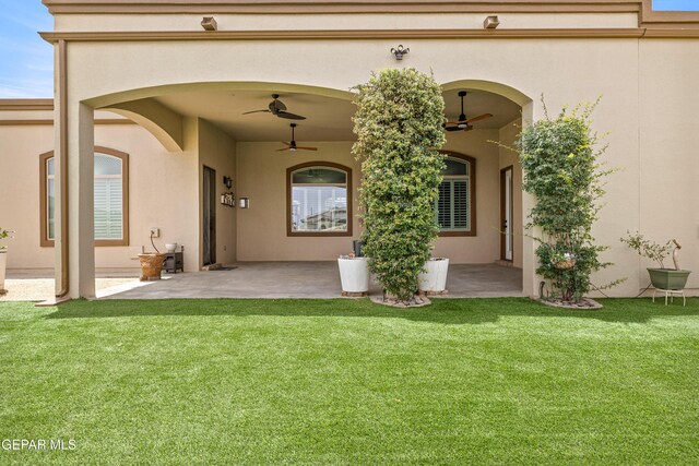 entrance to property featuring a ceiling fan, a lawn, a patio, and stucco siding