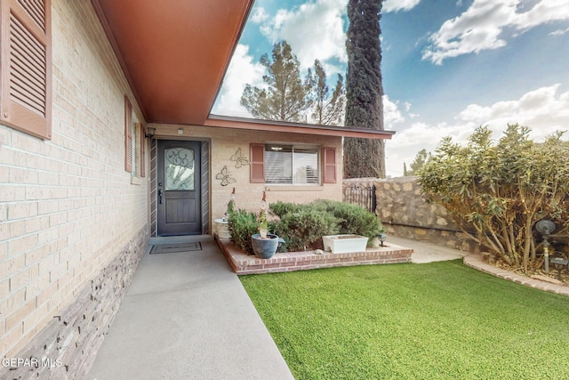 view of exterior entry featuring a lawn and fence