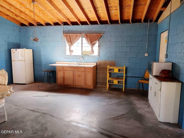 basement with concrete block wall, freestanding refrigerator, and a sink