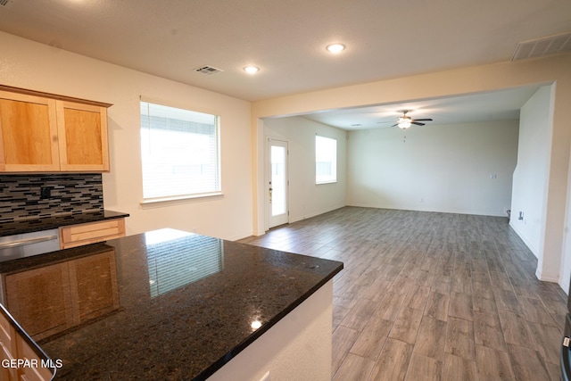 kitchen featuring visible vents, backsplash, dark stone counters, light wood finished floors, and ceiling fan