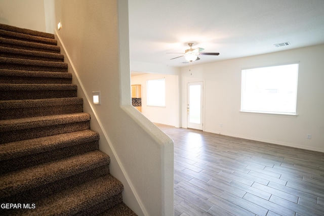 stairs featuring visible vents, a healthy amount of sunlight, wood finished floors, and a ceiling fan