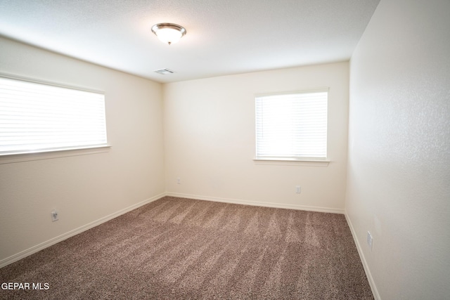 empty room featuring a wealth of natural light, visible vents, baseboards, and carpet