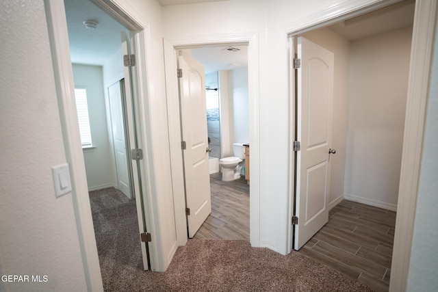 hall with visible vents, baseboards, and wood finished floors