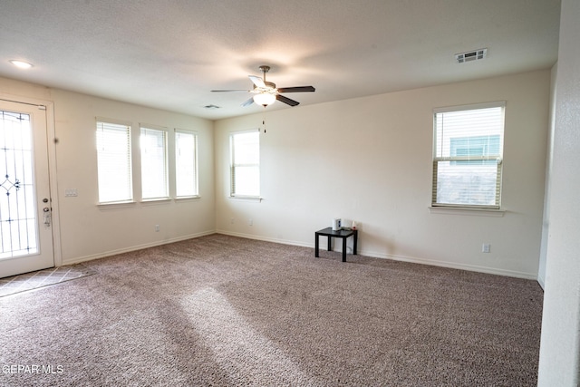 carpeted spare room with a textured ceiling, a ceiling fan, visible vents, and baseboards
