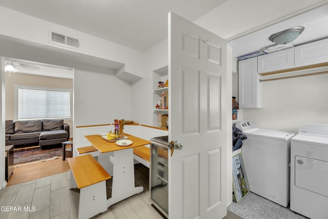 laundry room with light wood-type flooring, visible vents, wine cooler, cabinet space, and washing machine and clothes dryer