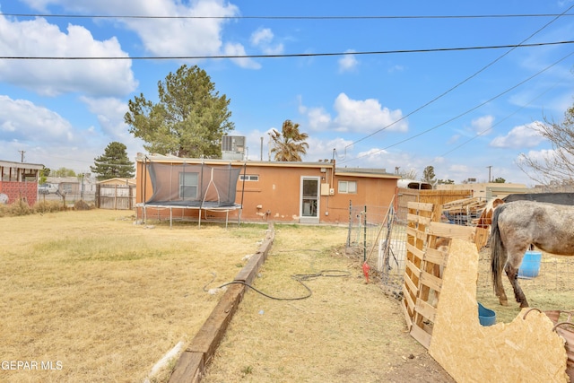 back of property with stucco siding, a lawn, a trampoline, fence, and cooling unit