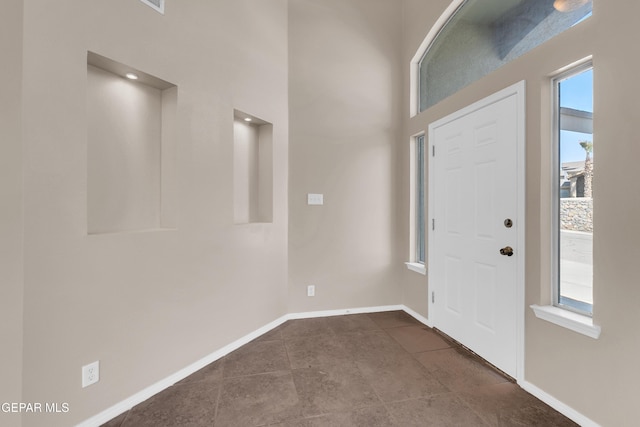 foyer entrance with dark tile patterned floors, baseboards, and a towering ceiling