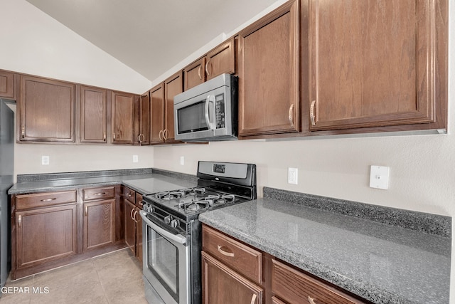 kitchen with dark countertops, appliances with stainless steel finishes, lofted ceiling, and light tile patterned flooring