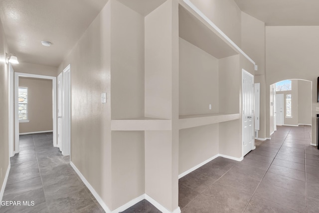 hall featuring baseboards, arched walkways, and tile patterned flooring