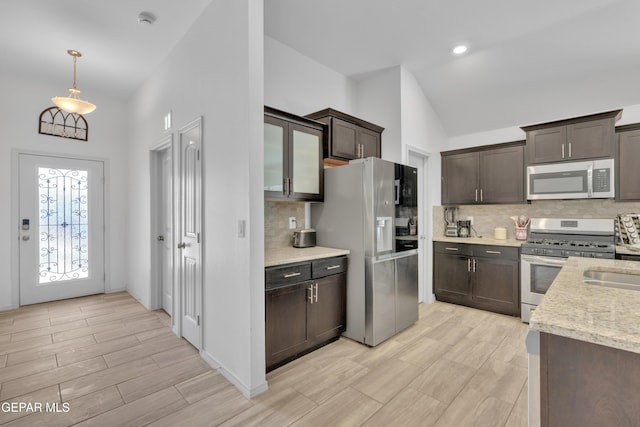 kitchen featuring dark brown cabinetry, tasteful backsplash, light stone counters, lofted ceiling, and stainless steel appliances