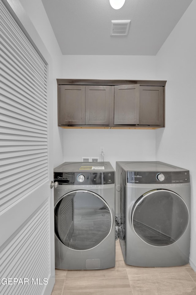 clothes washing area with light wood finished floors, visible vents, washer and clothes dryer, and cabinet space