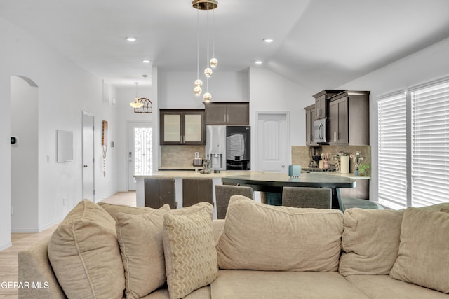 living room with light wood-type flooring, baseboards, recessed lighting, high vaulted ceiling, and arched walkways