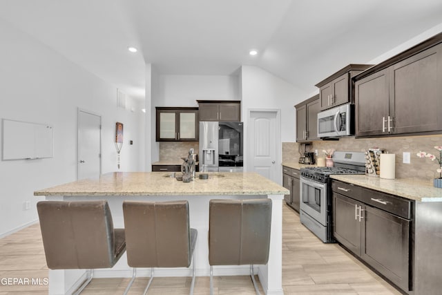 kitchen featuring dark brown cabinetry, backsplash, light stone counters, and appliances with stainless steel finishes