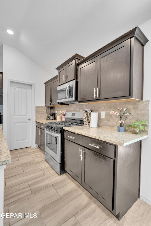 kitchen featuring wood finish floors, dark brown cabinets, lofted ceiling, stainless steel appliances, and decorative backsplash