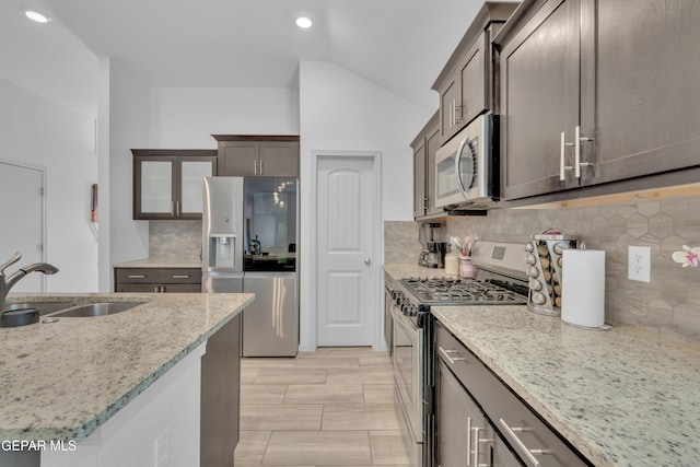 kitchen with tasteful backsplash, dark brown cabinetry, light stone counters, stainless steel appliances, and a sink