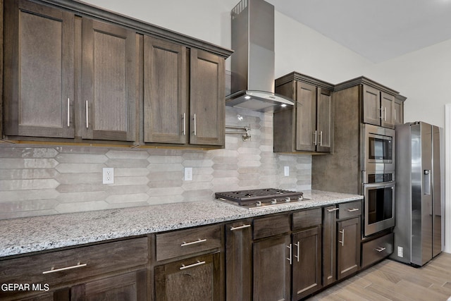 13095 Emerald Isle St, El Paso, TX 79928 - kitchen with stainless steel appliances, wall chimney range hood, dark brown cabinets, light stone countertops, and light wood finished floors
