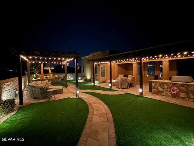 yard at night with a pergola, a patio area, exterior kitchen, and an outdoor hangout area