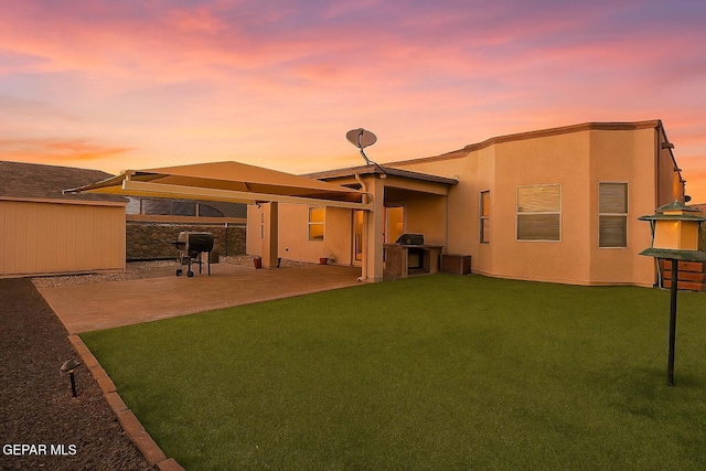 back of house at dusk with a shed, a yard, a patio, stucco siding, and an outbuilding