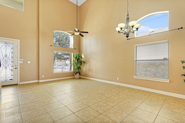 interior space featuring light tile patterned floors, a towering ceiling, ceiling fan with notable chandelier, and baseboards