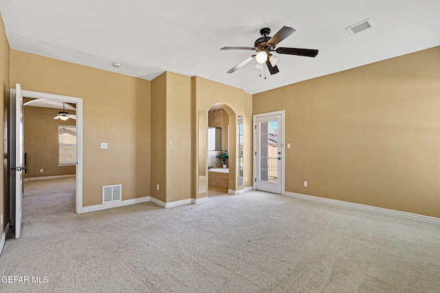 interior space with a ceiling fan, arched walkways, light colored carpet, and visible vents