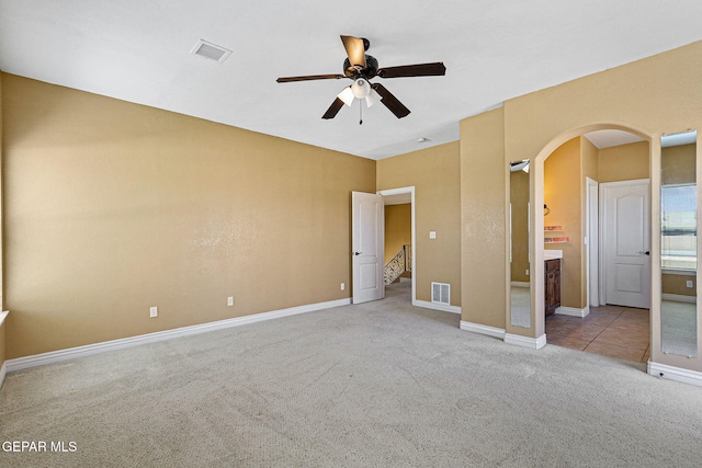 unfurnished bedroom featuring baseboards, visible vents, arched walkways, and carpet floors