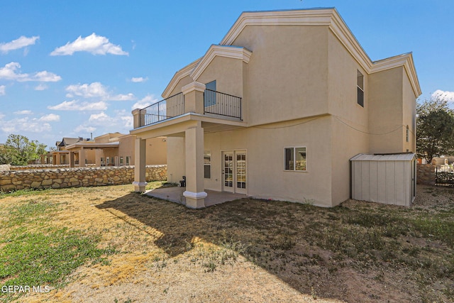 back of property with a patio area, french doors, stucco siding, a balcony, and a lawn