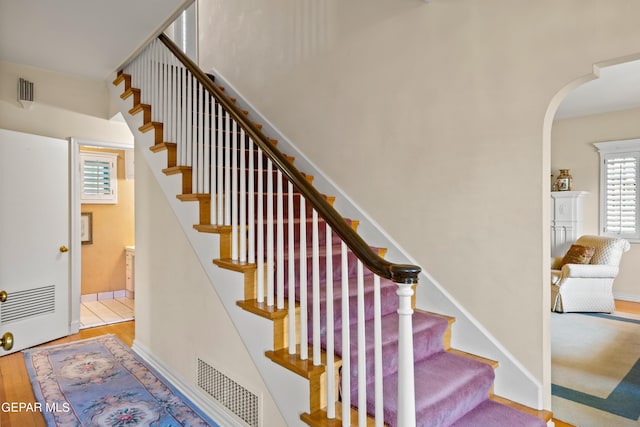 stairs featuring wood finished floors, arched walkways, baseboards, and visible vents