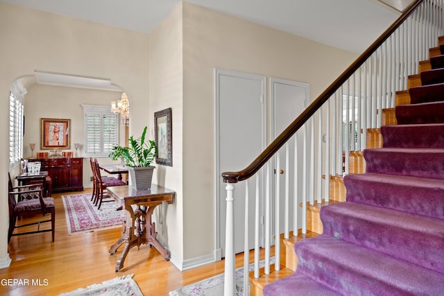 stairway with arched walkways, baseboards, a notable chandelier, and wood finished floors