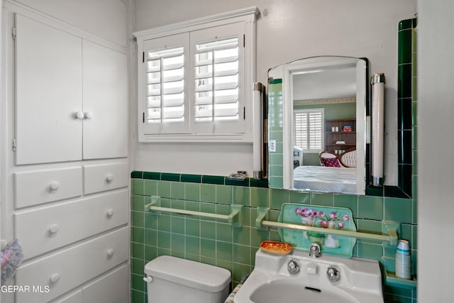ensuite bathroom featuring toilet, a wainscoted wall, ensuite bath, and tile walls