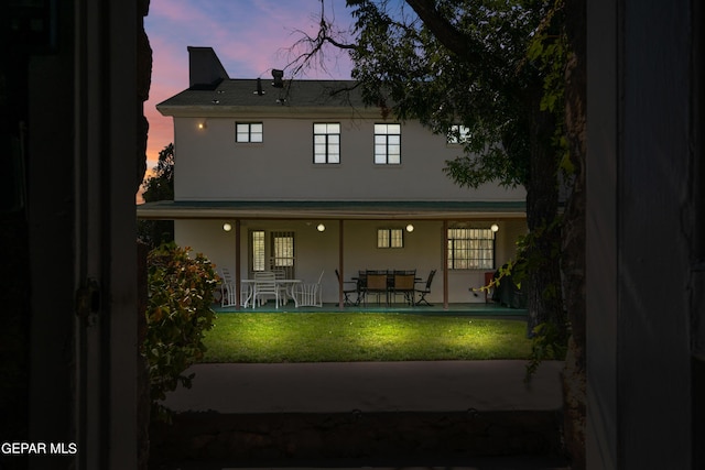 back of house at dusk featuring a patio, stucco siding, and a yard