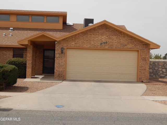 view of front of property featuring an attached garage, driveway, brick siding, and central AC