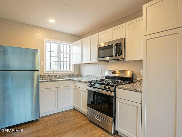 8718 Lawson St Unit 9, El Paso, TX 79904 - kitchen featuring stainless steel appliances, white cabinetry, a sink, stone counters, and light wood-style floors