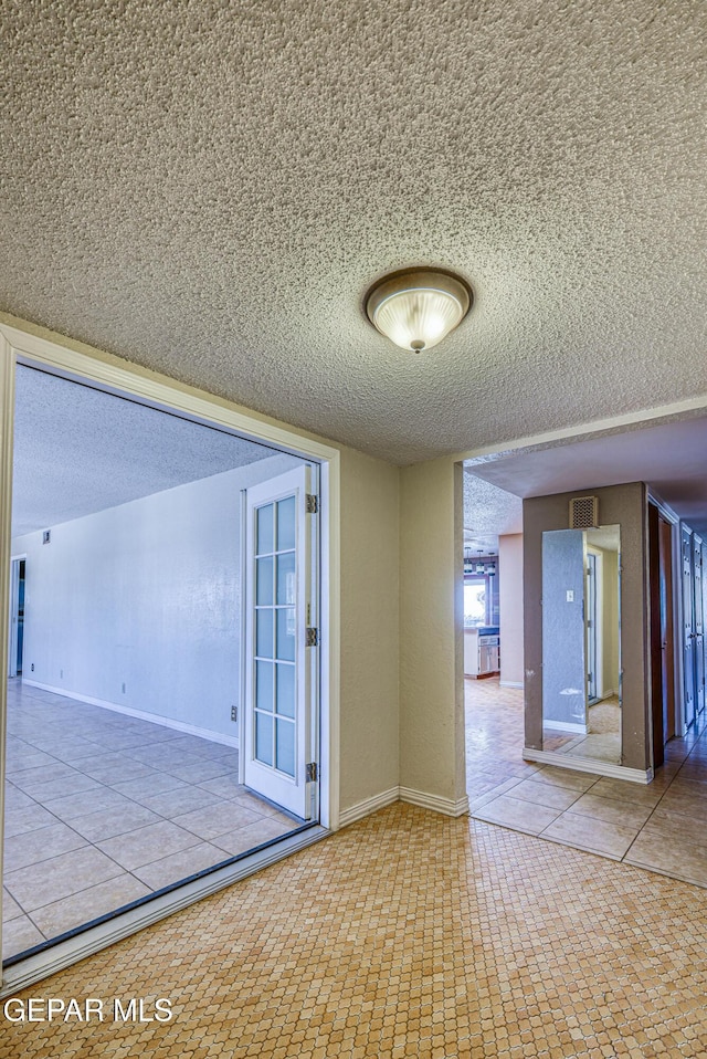 empty room featuring a textured ceiling, visible vents, baseboards, and tile patterned flooring