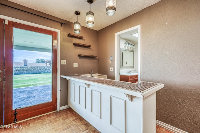 bathroom featuring baseboards, a textured ceiling, a textured wall, and a sink