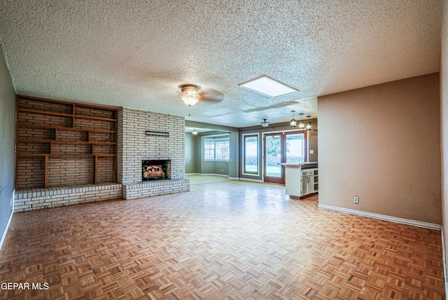 unfurnished living room with a fireplace, baseboards, a textured ceiling, a ceiling fan, and a skylight