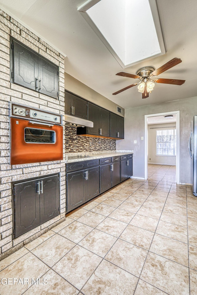 kitchen with light tile patterned flooring, ceiling fan, light countertops, freestanding refrigerator, and wall oven